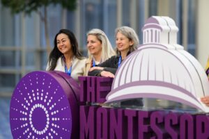 three women standing behind a 3D logo at The Montessori Event