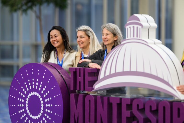 three women standing behind a 3D logo at The Montessori Event